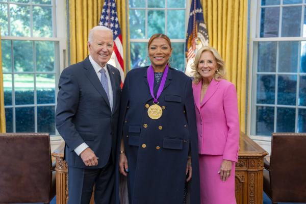 Black woman in blue jacket wearing a medal around her neck surrounded by older man wearing a blue suit and woman with blonde hair wearing a pink suit.
