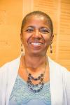 Photo of Akua Kouyate Tate wearing a blue top, white sweater, long earrings and a matching necklace with blue beads.
