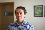 Portrait of Asian man in blue striped shirt with a door and a painting in the background.