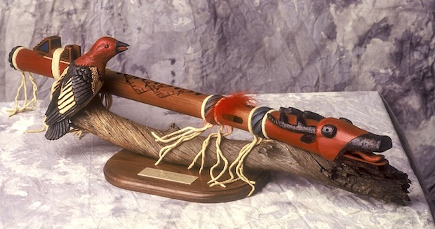 An ornate wooden flute on a rest with a carved bird.